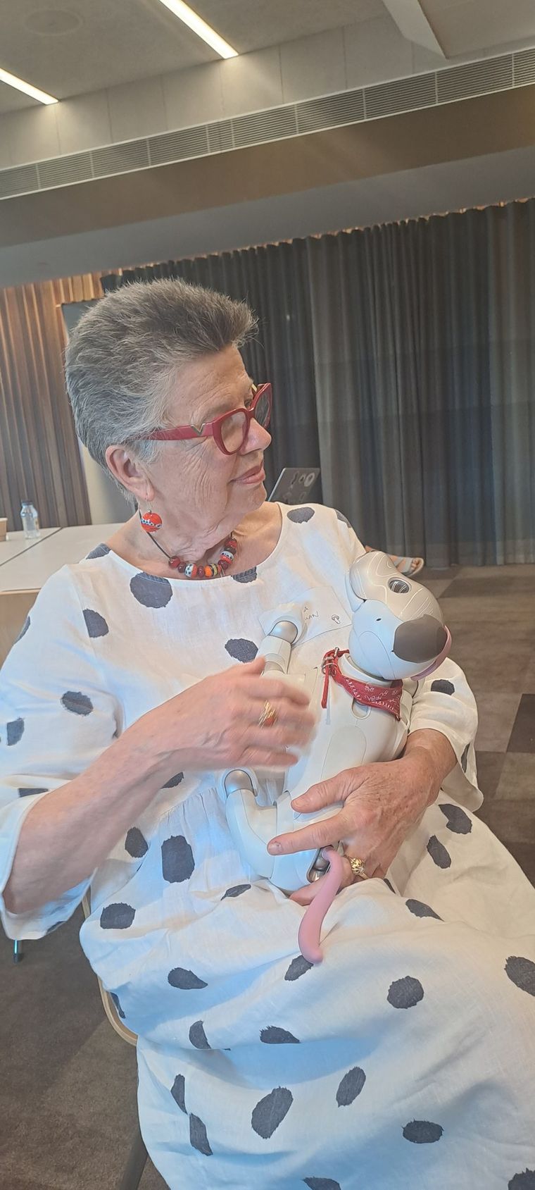 A workshop participant in a spotted linen dress holding a Sony Aibo robot dog on her lap.